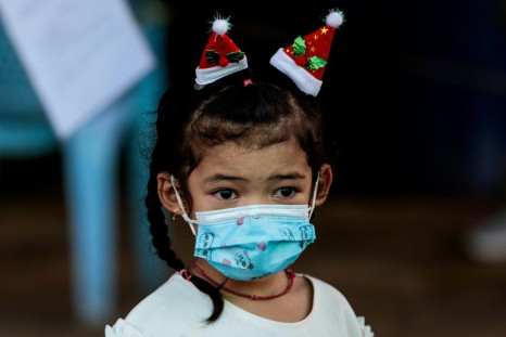 A girl wearing a face mask and Santa Claus hats watches as medical officials test people for coronavirus at the seafood market