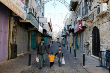 Children walk by shuttered shops in a street decorated ahead of Christmas in Bethlehem in the occupied West Bank amid the novel coronavirus pandemic crisis