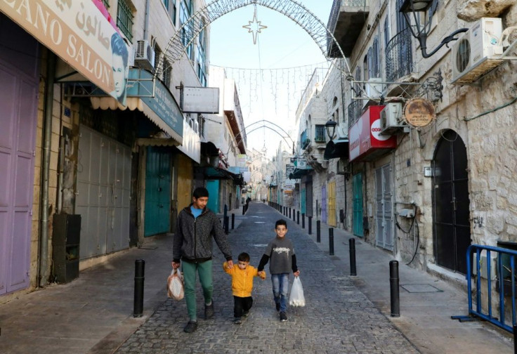 Children walk by shuttered shops in a street decorated ahead of Christmas in Bethlehem in the occupied West Bank amid the novel coronavirus pandemic crisis