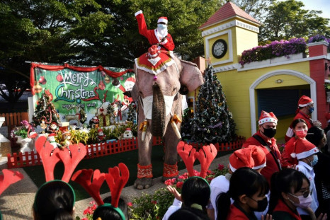 An elephant from the Ayutthaya Elephant Palace, dressed in a Santa Claus costume and wearing a face mask, is greeted by students during an event to hand out masks at a school in Ayutthaya, Thailand