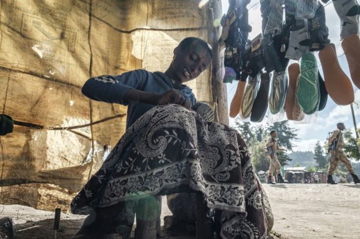 A cobbler in Korem, a town north of Alamata, repairs a shoe as soldiers of the Amhara special forces walk by