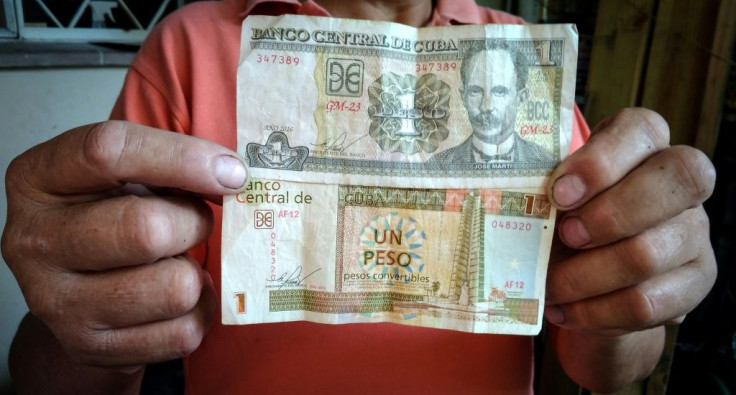 In this file photo taken on February 8, 2018 a Cuban worker shows 1 CUP (Cuban peso - top) and 1 CUC (Cuban convertible peso - bottom) in Havana