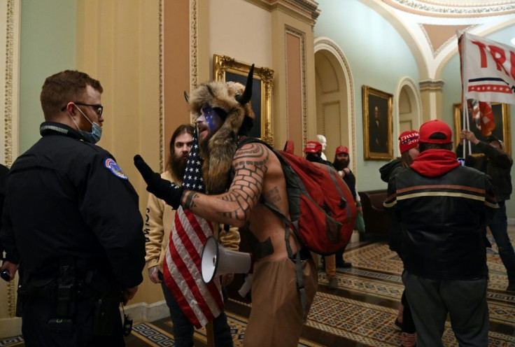 A US Capitol police officer talks to supporters of US President Donald Trump, including Jake Angeli (R), a QAnon supporter known for his painted face and horned hat, that entered the Capitol on January 6 as part of a violent protest