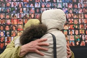 Grieving relatives in front of a huge screen displaying photos of the 176 people killed when a Ukraine International Airlines flight was downed a year ago. The first-year anniversary event was held at the site of a future memorial in Kiev