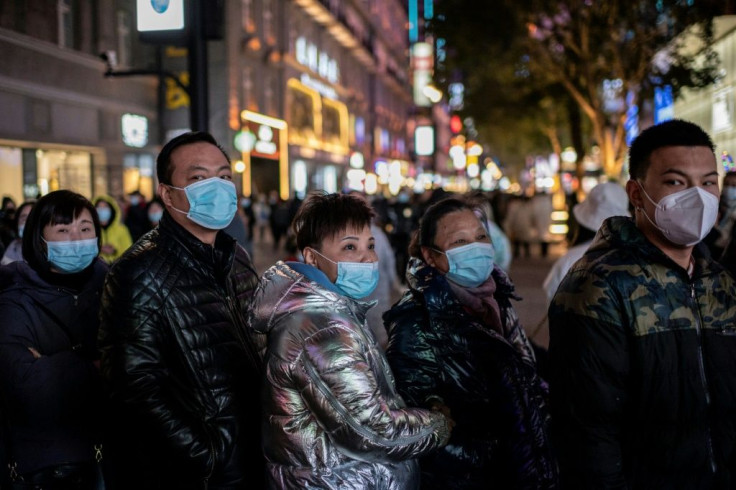 People wearing face masks stand around a giant 3D screen on Jianghan street in Wuhan on January 10, 2021, the eve of the first anniversary of China confirming its first death from the Covid-19 coronavirus