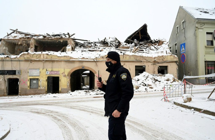 A policeman stands in front of snow-covered ruins in Petrinja