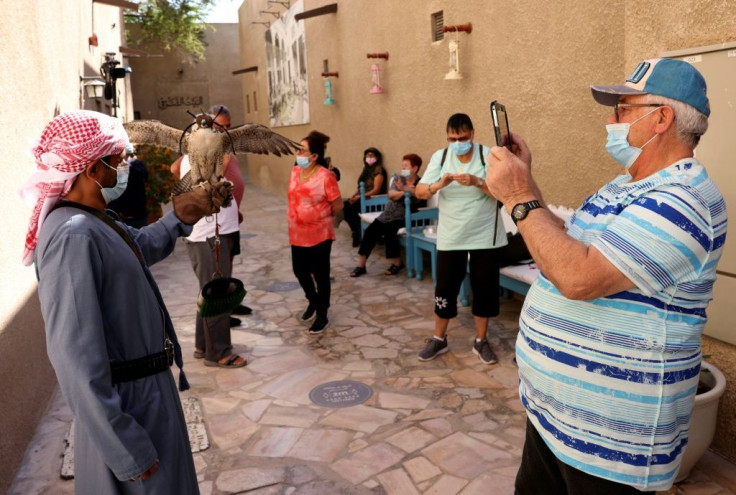 A mask-clad Israeli tourist photographs a falconer holding a falcon during a visit to Dubai's historic district