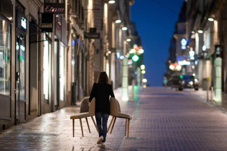 A woman holding chairs walks down an empty street in Nantes, France during the nationwide 6 pm curfew