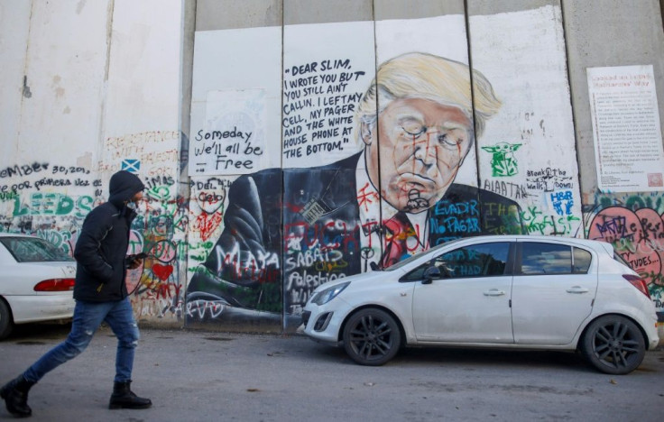 A Palestinian walks past a defaced mural painting of former US president Donald Trump on Israel's controversial separation barrier, which divides the West Bank from Jerusalem