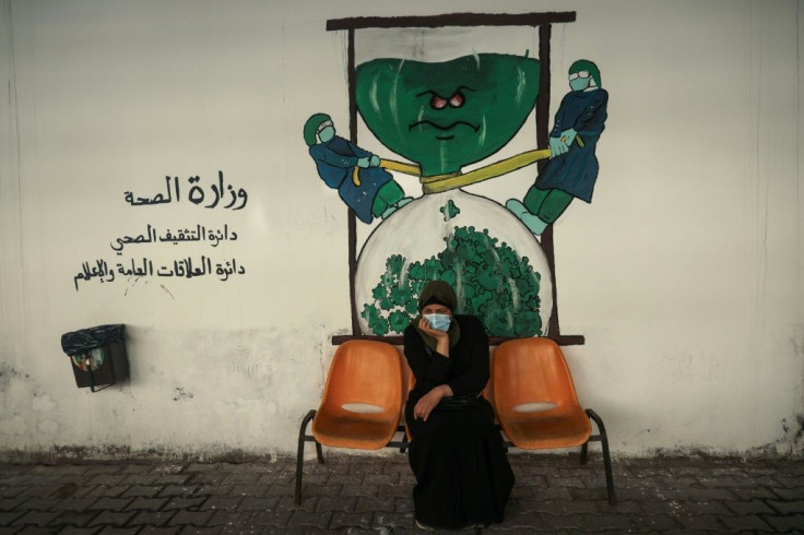 Tahani al-Rifi sits on a bench in front of a coronavirus-inspired mural in Gaza, from where she is unable to leave to receive treatment for cancer