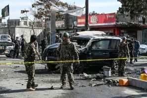 Afghan security personnel surround a vehicle hit by a bomb that killed two people, including a Kabul district police chief