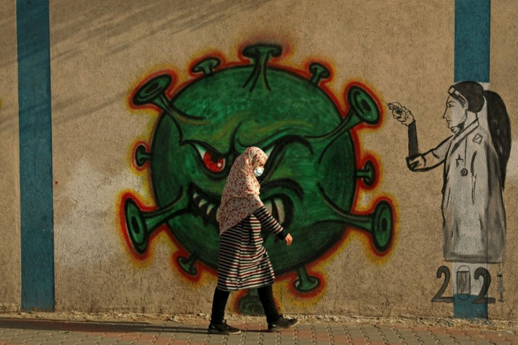 A Palestinian woman, wearing a protective mask amid the COVID-19 pandemic, walks past a coronavirus-inspired mural in Gaza City