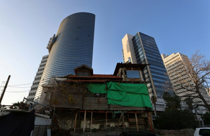 An old wooden house stands in front of modern buildings in the Israeli coastal city