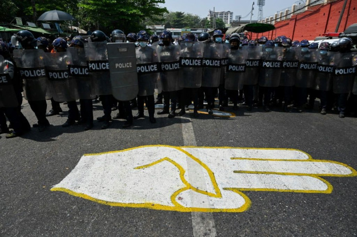 Riot police guard a road in Yangon Thursday in front of a street mural of a three-finger salute popular among anti-coup protesters