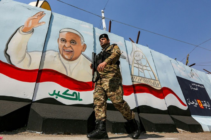 A member of the Iraqi security forces walks past a mural of Pope Francis with an Iraqi national flag, painted on a blast wall outside the Syriac Catholic Church of Our Lady of Deliverance in Baghdad