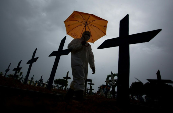 In this file photo taken on February 25, 2021 a worker wearing a protective suit and carrying an umbrella walks past the graves of Covid-19 victims at the Nossa Senhora Aparecida cemetery, in Manaus, Brazil