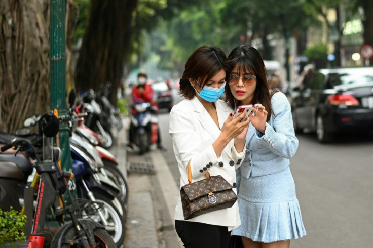 Insurance saleswoman Nguyen Thi Thanh Loan (R) checks her mobile phone after getting her photographs taken by a friend in Hanoi, a day after taking the course