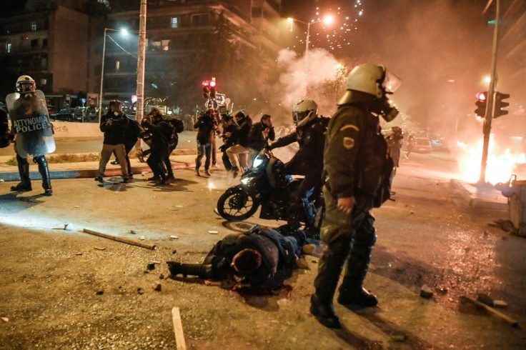 Police stand around a fellow officer laying in the street after being badly injured by protesters demonstrating against police violence in an Athens suburb