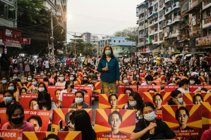 Anti-coup protesters with images of detained leader Aung San Suu Kyi sit along a street in Yangon