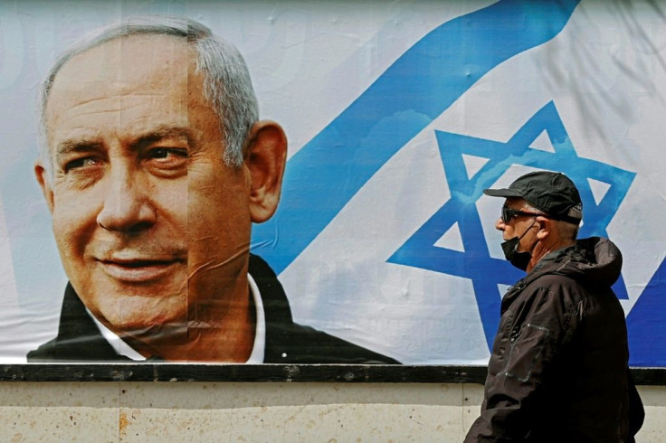 People walk past an electoral billboard for Israel's Likud party bearing a portrait of its leader Prime Minister Benjamin Netanyahu who faces the fourth election in under two years