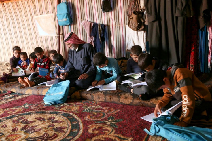 Syrian Abderrazaq Khatoun helps some of his 11 orphaned grandchildren with their school work inside a tent they call come in an encampment in the northwestern Syrian province of Idlib