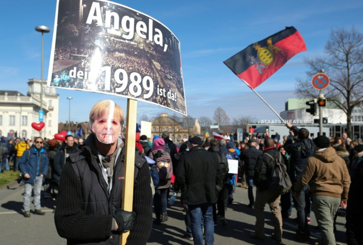 A masked protester holds a placard reading "Angela, your 1989 has come"