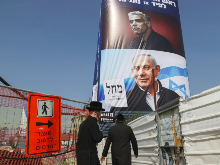 Ultra-Orthodox Jews walk past an election campaign poster bearing the image of opposition leader Yair Lapid (top) and Prime Minister Benjamin Netanyahu (bottom), in the central Israeli city of Bnei Brak