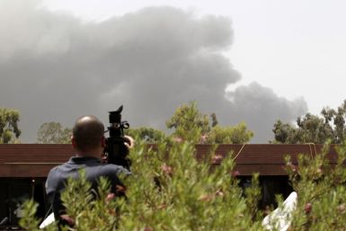 A journalist films from the roof of a hotel as smoke rises in the sky in Tripoli