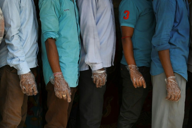 Voters wearing plastic gloves stand in a line to cast their vote outside a polling station during Phase 2 of West Bengal's legislative election in Nandigram