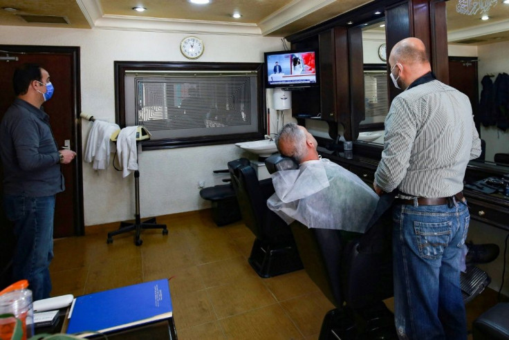 Jordanians follow the latest political developments in their country on a television set inside an Amman barber shop
