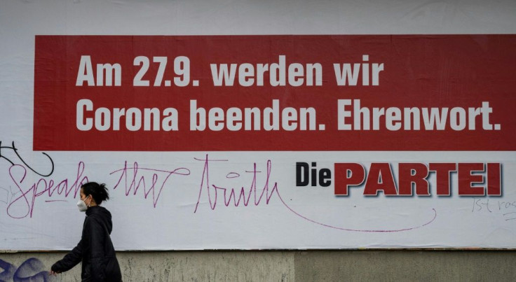 A woman walks past an election campaign poster for the satirical German political party 'Die Partei' reading 'On the 27th of September, we will put an end to Corona - Promise'