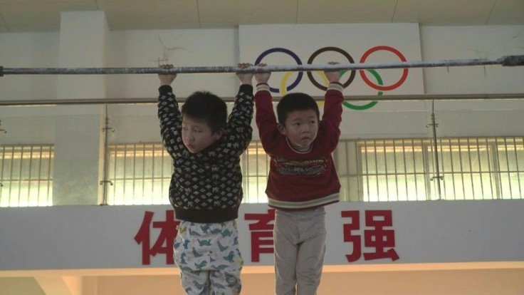 Under the twin emblems of the Chinese flag and the Olympic rings, two tiny boys dangle from the high bar in a cavernous gymnasium -- the cradle of China's elite gymnasts.