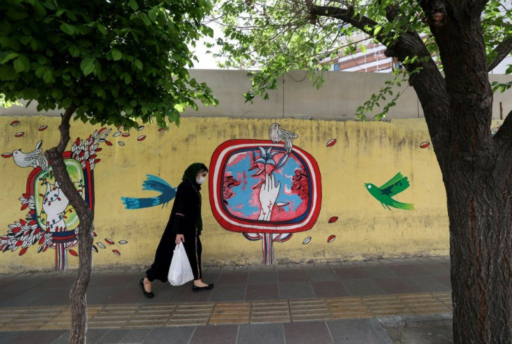 An Iranian woman walks next to a mural-covered wall on a street in the capital Tehran