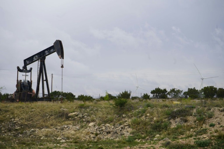 Blades from wind turbines rotate in a field behind an out-of-use oil pumpjack near Eldorado, Texas