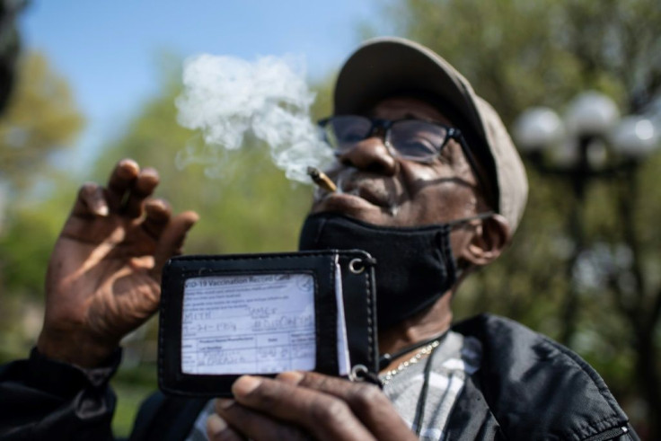 A man smokes a joint and shows his vaccination card as marijuana activists hand out free joints to vaccinated New Yorkers on April 20, 2021 in New York City