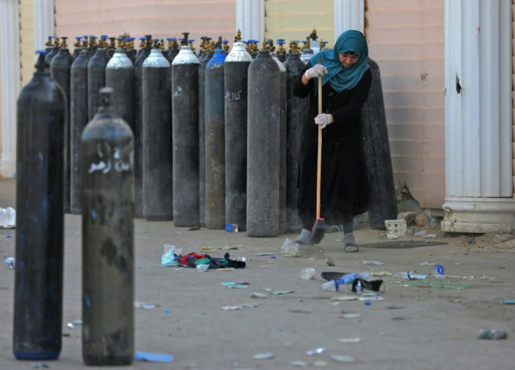 An Iraqi woman cleans debris next to evacuated oxygen bottles outside the Ibn al-Khatib Hospital in Baghdad, on April 25 after a fire broke out there killing at least 23 people