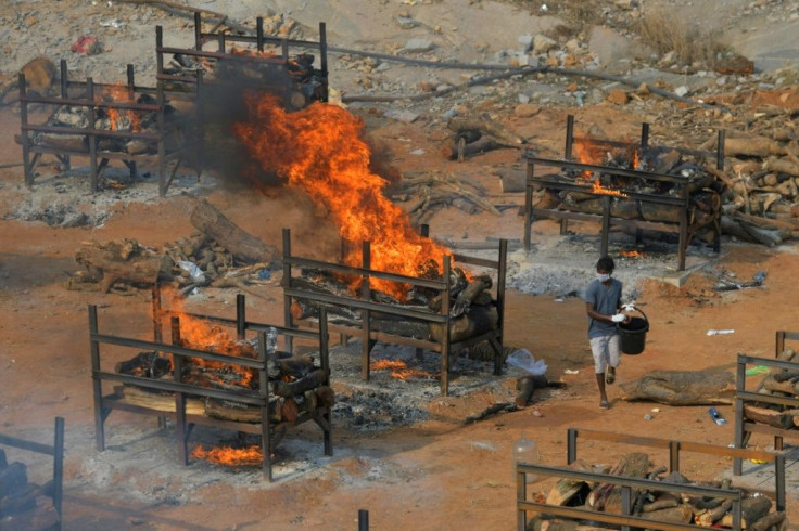 An undertaker walks by burning pyres for victims who died of Covid-19 at an open-air crematorium in Bangalore