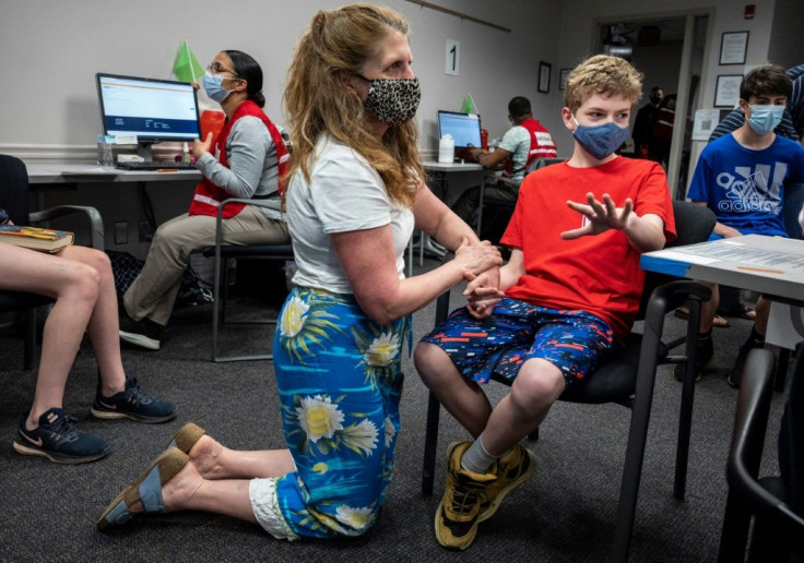 Elizabeth Brauer (C) holds the hand of her son Luke Brauer, 13, before he receives a Covid-19 vaccination at the Fairfax Government Center vaccination clinic in Fairfax, Virginia