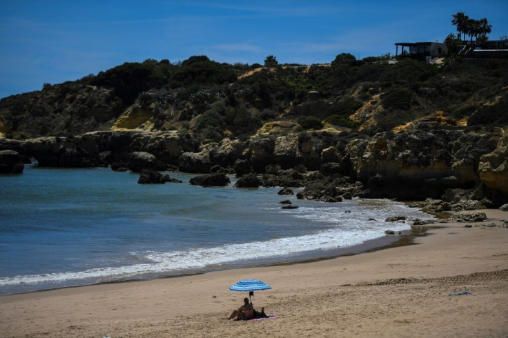 A woman sits under a beach umbrella at Oura beach. Restaurant owners and others hailed the restart of tourism, but some were cautious