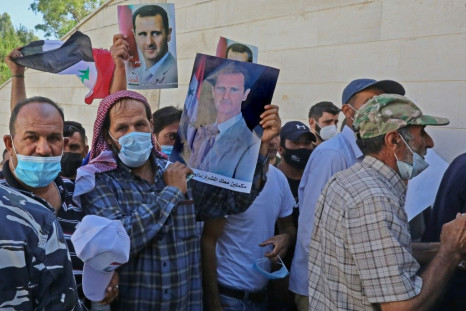 Syrian residents of Lebanon hold portraits of Bashar al-Assad, as they queue outside the embassy to cast early ballots for next Wednesday's presidential election which is expected to give the veteran incumbent a new term