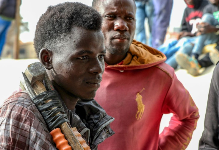An African migrant labourer rests tools on his shoulder as he waits for work under a bridge in Tripoli