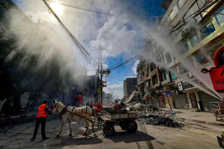 Water is sprayed to reduce dust in the air as volunteers clean up the streets in the Al-Remal commercial district in Gaza City following Israeli air strikes