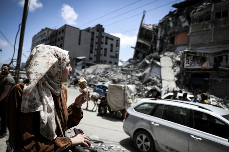 A Palestinian woman eats ice cream in front of the Al-Shuruq building destroyed by an Israeli air strike
