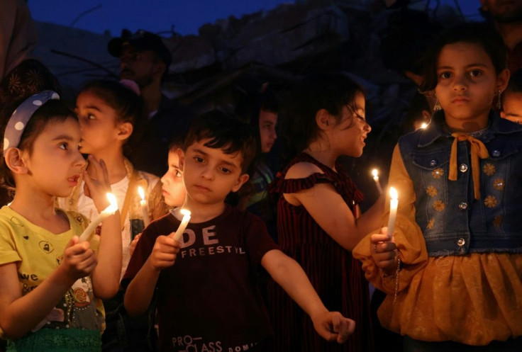 Palestinian children hold candles during a rally amid the ruins of houses destroyed by Israeli strikes in Gaza City on May 24