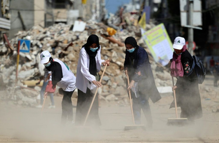 Palestinian volunteers sweep the rubble of buildings, recently destroyed by Israeli strikes, in Gaza City's Rimal district