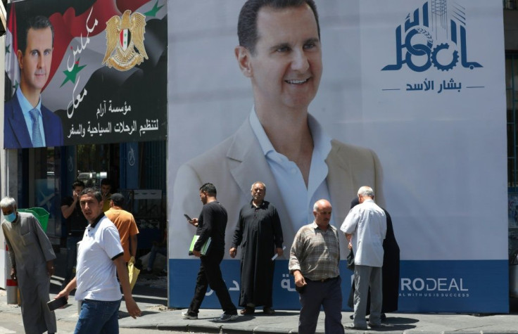 People walk by election campaign billboards depicting Syrian President Bashar al-Assad