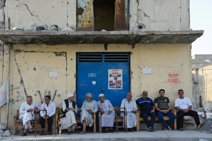 Iraqi men sit in the shade next to a building in the city of Mosul, on May 26, 2021, destroyed during fighting with the Islamic State group jihadists in the 2017 battle for the city