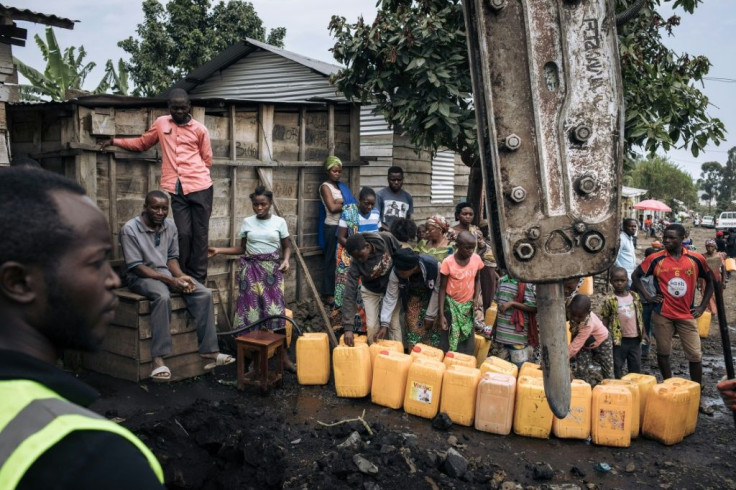 Goma residents collect water while workers repair power lines destroyed by the lava flow from the Nyiragongo volcano