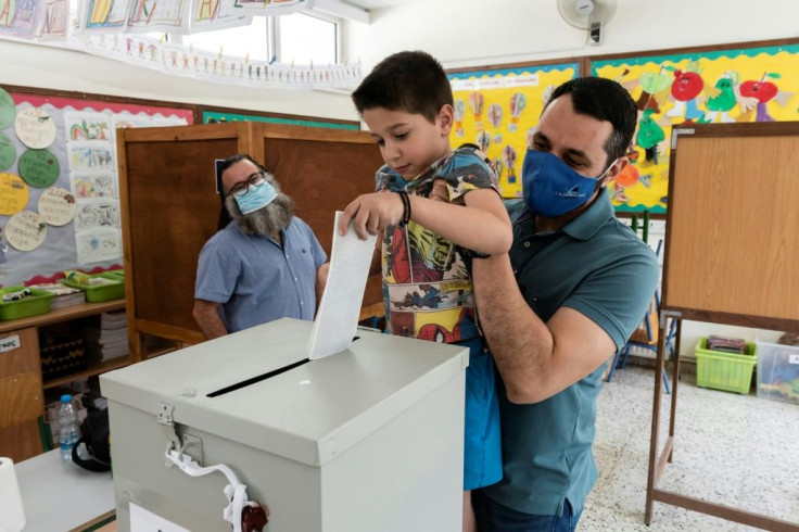 A Cypriot man holds his son up to cast his ballot at a polling station in Nicosia on May 30, 2021