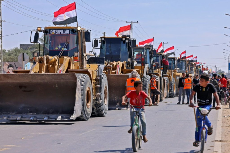 Palestinian boys cycle past a convoy of bulldozers provided by Egypt arriving at the Palestinian side of the Rafah border crossing between Egypt and the Palestinian Gaza Strip enclave on June 4, 2021